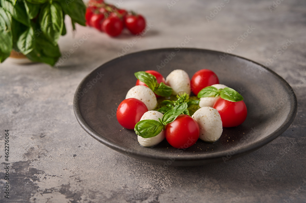 Delicious caprese salad with ripe tomatoes, fresh basil and mozzarella cheese in black plate on the background as concrete. Close up Delicious caprese salad with ripe tomatoes, fresh basil and mozzarella cheese in black plate on the background as concrete. Close up