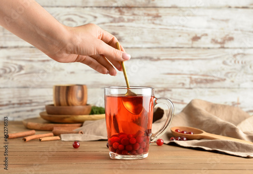 Woman preparing tasty cranberry tea on wooden table