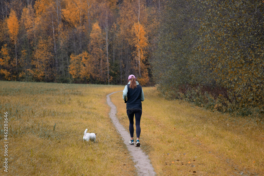 A woman with a dog in the park is running. Sports on the street. A woman with a dog in the park is running. Sports on the street.