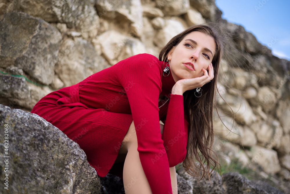 Young girl in the red dress is sitting on stone among the ancient ruins. Young girl in the red dress is sitting on stone among the ancient ruins.