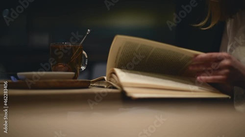 Modern female in formal outfit studies in cozy atmosphere cafe with book and cup of tea in the late evening. Education with pleasure with warm drink reading book.