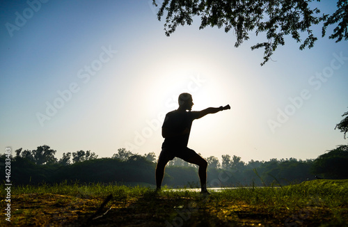 silhouette of a boy doing taekwondo kicks practice in park near sun and river 
