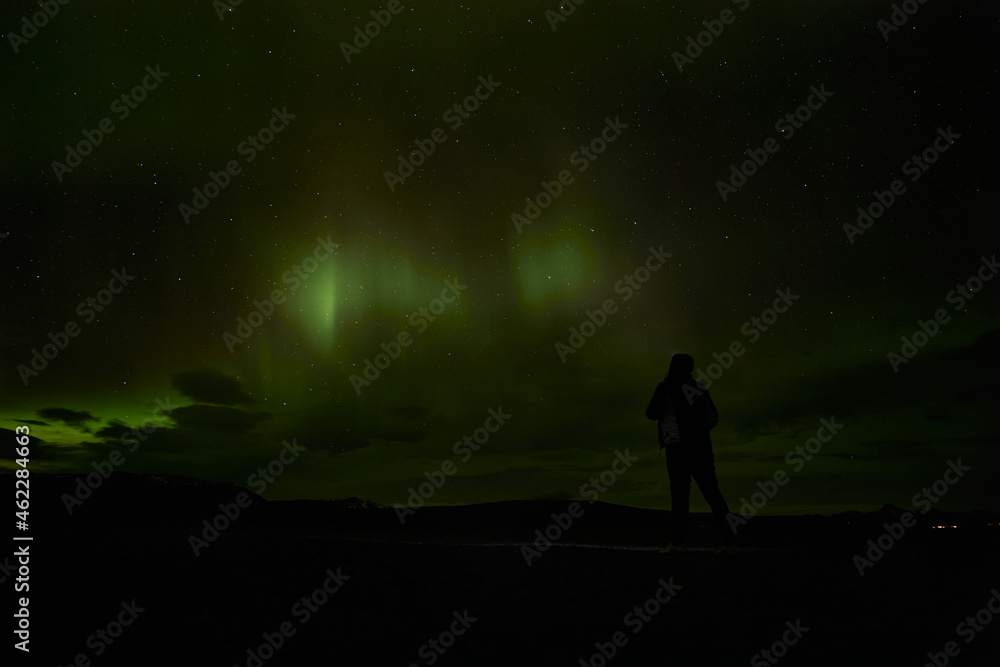 Silhouette of woman watching night sky with aurora borealis