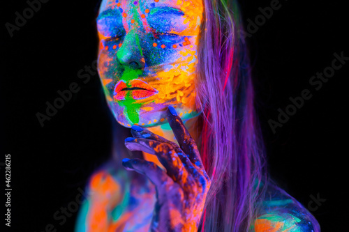 Beautiful young woman in neon light. Portrait of a model with fluorescent makeup posing in UV light with colorful makeup