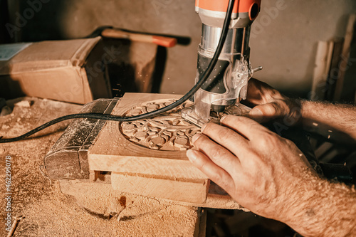 A carpenter craftsman carves wood using an automated tool according to a previously prepared pattern. Close-up on skill hands at work