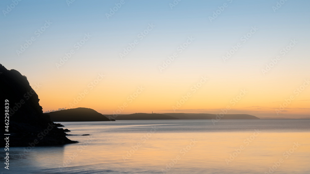 Beautiful sunrise over Pentewan Sands in Cornwall with pastel sky and long exposure ocean