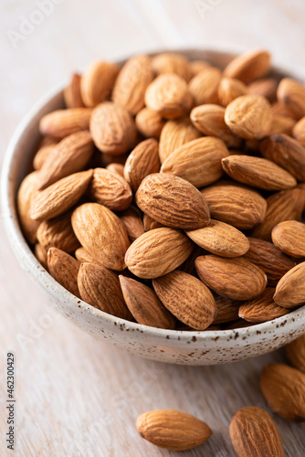Almonds in a bowl on a wooden background, closeup view. Healthy raw vegan food