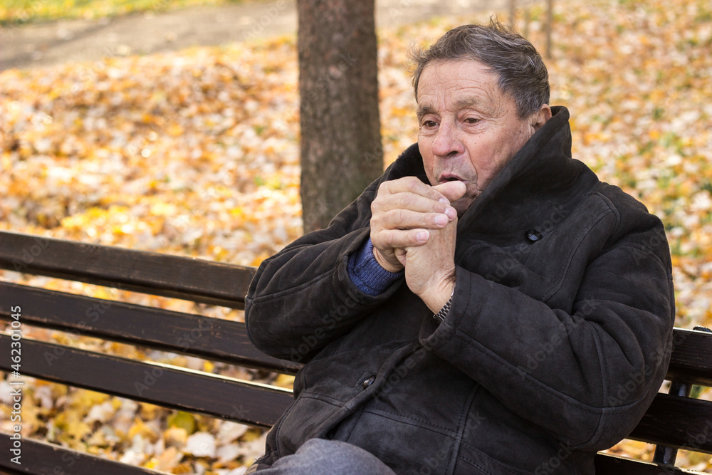 Senior man breathing on his hands to keep them warm Senior man breathing on his hands to keep them warm