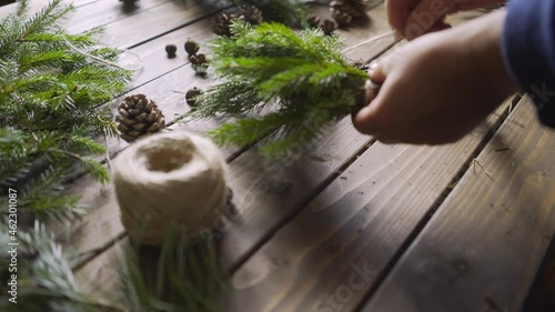 Aged wooden table in authentic florist workshop. Motion shot close-up female hands use and attach evergreen fir branches, preparing handmade xmas decoration. DIY and handcraft concept