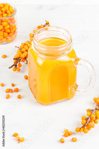 Yellow juice in a glass mug. Close-up on a white background, with sea buckthorn twigs.