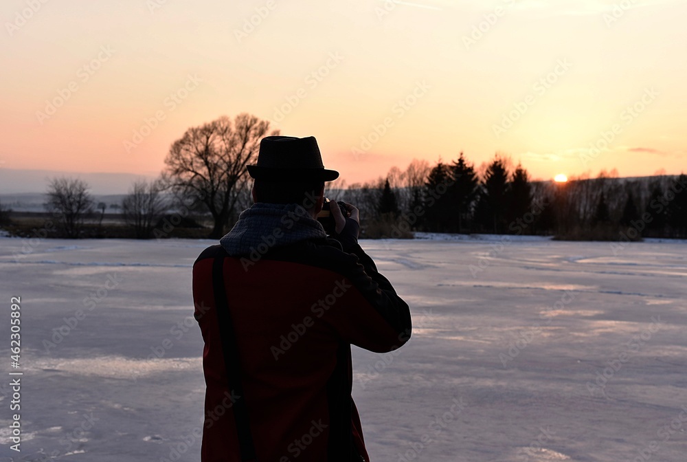 man photographs the sunset in a snowy landscape