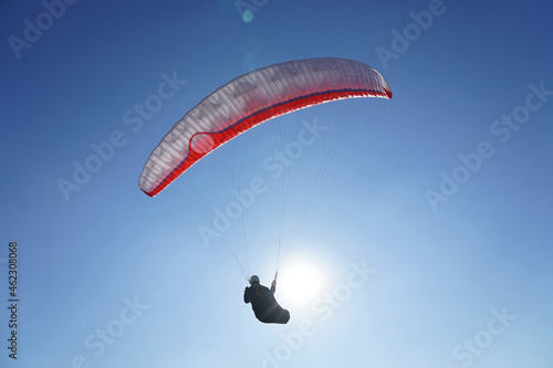A paraglider flies a glider against a blue sky in good sunny weather. Close up