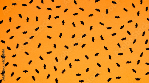 Many black paper bats on a bright orange background, seamless drawing, pattern.Concept for a holiday card, Halloween banner, top view, flat lay.Festive decor.