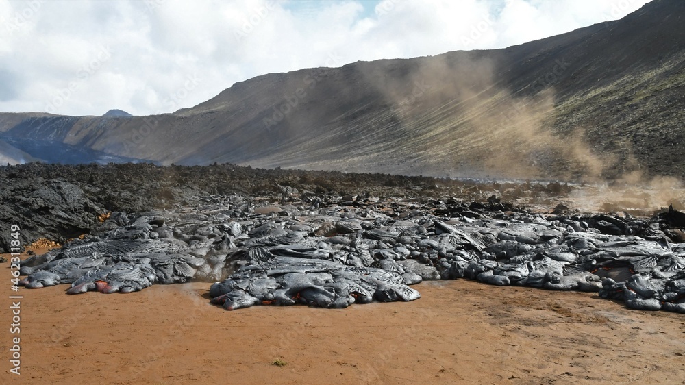 Pahoehoe lava flow at Nátthagi valley in Iceland. Lava crust is gray and black, molten lava is red. Mountain in the background, and dusty steam rises from the lava.