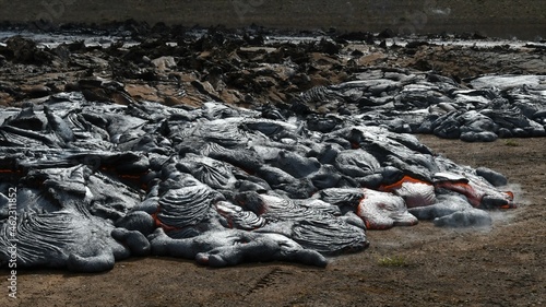 Pahoehoe lava flow at Fagradalsfjall, Iceland. Lava crust is gray and black, molten lava is red and orange. Steam and gas are visible.