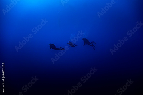 Three Scuba divers silhouette swimming in deep blue
