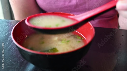 bowl of Japanese miso soup being spooned out by young woman at restaurant eating fancy authentic cuisine with sea weed and tofu photo