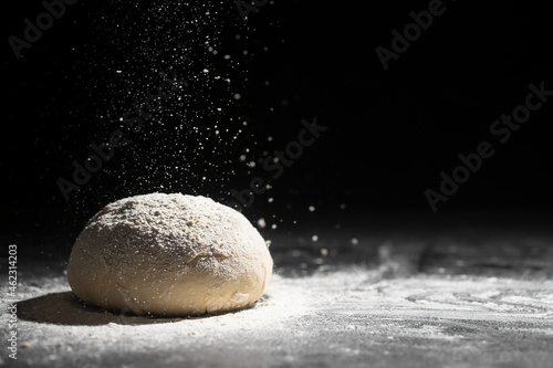 Yeast dough with pouring flour on a dark background