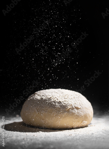 Yeast-free dough with pouring flour on a dark background