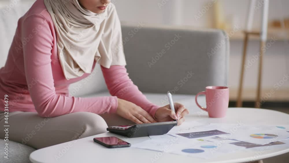 Unrecognizable muslim woman working at home, calculating finances and taking notes, making business plan, free space Unrecognizable muslim woman working at home, calculating finances and taking notes, making business plan, free space