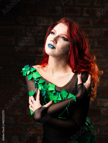 poison ivy comics character cosplay. Halloween costume. young sexy woman in a vine, leaves and poison ivy costume posing as a superhero against brick wall background. female with curly red hair