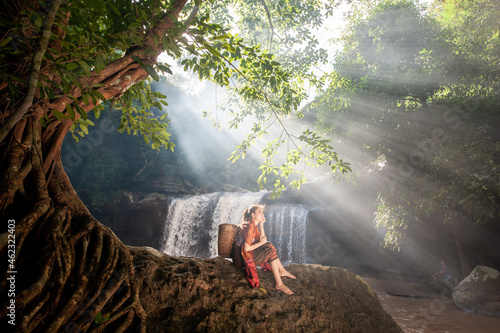 girl sitting on the rocks with a backdrop of a waterfall and light