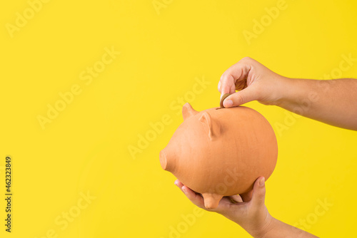 horizontal de las manos de una mujer sosteniendo una alcancía de un cerdo con dinero en fondo amarillo photo