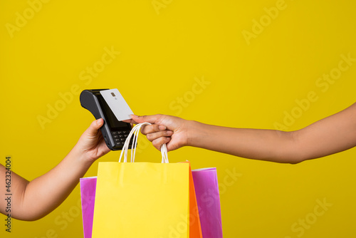 mano de una mujer pagando las compras con una tarjeta en un dispositivo inalámbrico en fondo amarillo