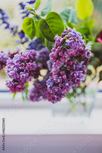 close-up of bunch of purple flowers including lillac in vase indoor by the window
