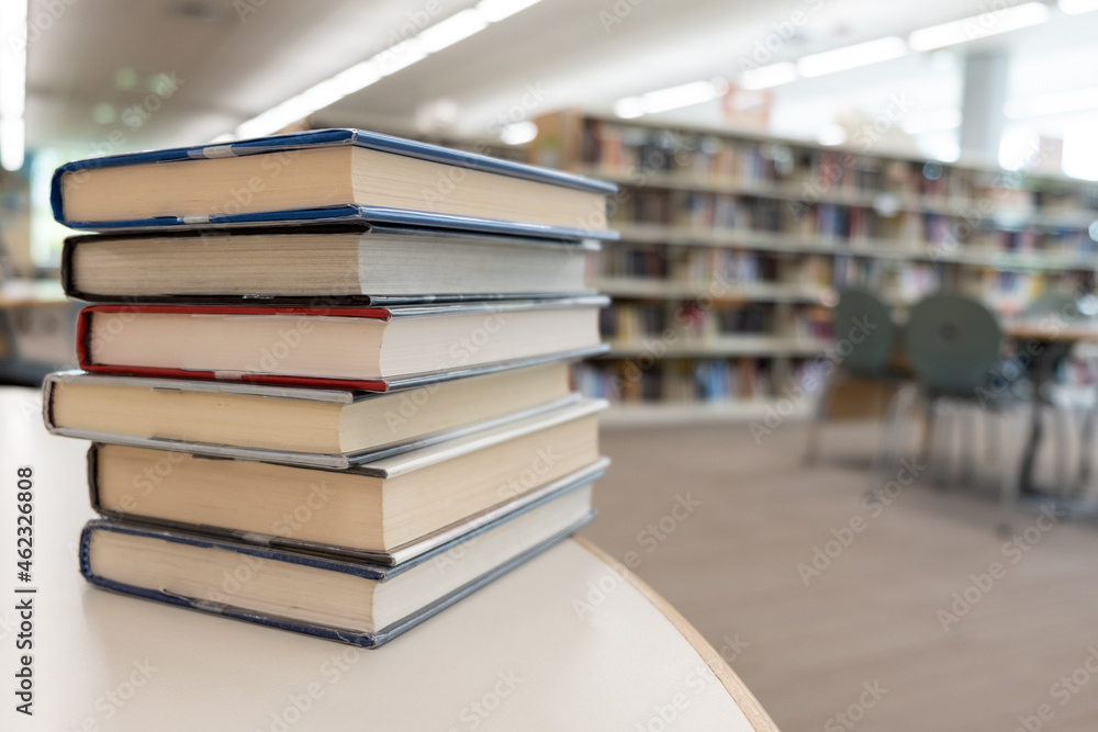 Stack of books on table against bookshelf at library for education, literature or wisdom concept Stack of books on table against bookshelf at library for education, literature or wisdom concept