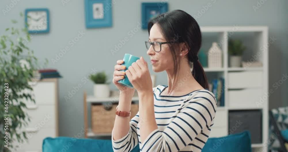 Happy caucasian woman with dark hair with glasses standing at home and enjoying beautiful view from window with cup of coffee. Happy caucasian woman with dark hair with glasses standing at home and enjoying beautiful view from window with cup of coffee.