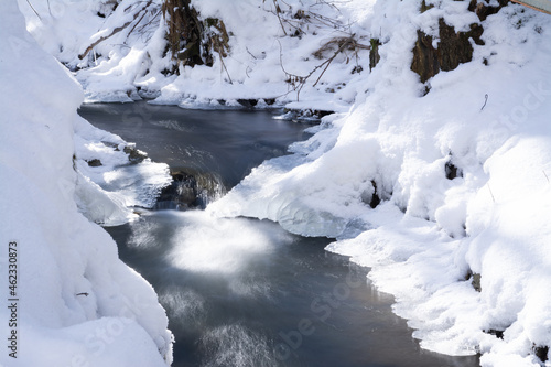 smooth motion of wild water in a river in winter with snow and ice on rocks and stones in the beautiful nature of a forest