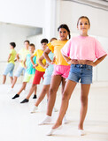 Cute preteen girl with group of children lined up one after another practicing ballet moves during choreography class in studio.