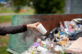 Woman throwing a cardboard glass into a recycling bin. Taking care of the cleanliness of the city and the environment. A large trash bin in a public park