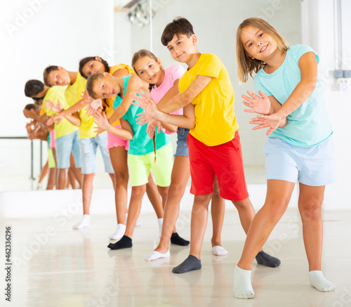 Принти на полотні Group of cheerful tween children standing in row one by one, learning movements of vigorous funny dance in choreography lesson