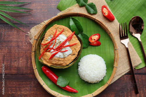 Steamed fish curry in banana leaf cups served with white rice - Famous Thai food called Hor Mok or fish Amok at top view on wooden background
