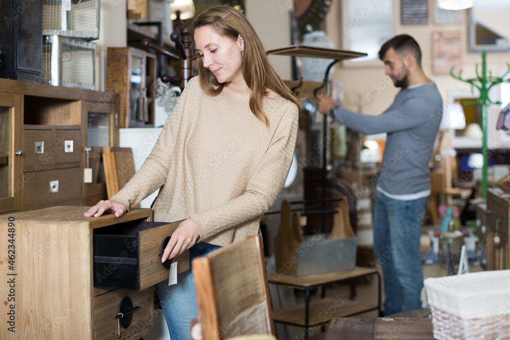 Young attractive girl choosing vintage bedside table in furnishings store