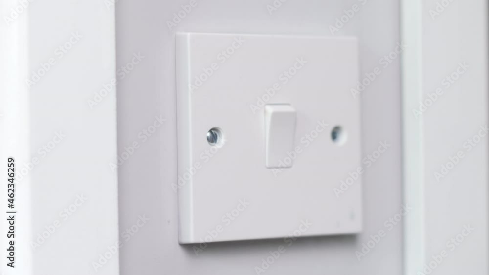 A light switch being turned by a man at night in a dark room A light switch being turned by a man at night in a dark room