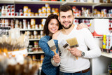 Happy young couple examining various painting brushes in paint supplies store
