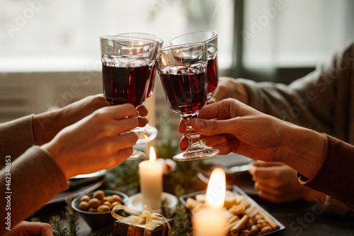 Close up of friends enjoying Christmas dinner together and toasting with wine glasses while sitting by elegant dining table with candles