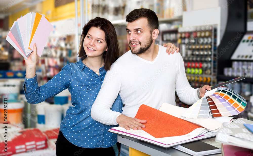 Cheerful young couple examining color scheme variants in paint supplies supermarket