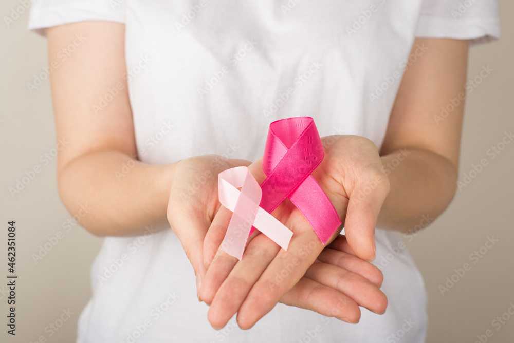 Photo of young woman in white t-shirt holding two pink ribbons in palms symbol of breast cancer awareness on isolated grey background Photo of young woman in white t-shirt holding two pink ribbons in palms symbol of breast cancer awareness on isolated grey background