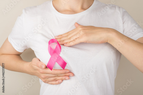 Photo of woman in white t-shirt with pink ribbon self examining her breasts on isolated grey background