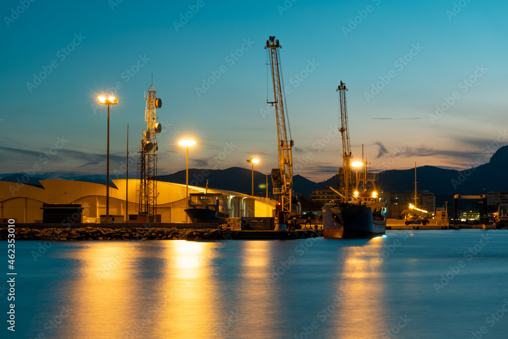 Long exposure night photo in a harbor overlooking ships and warehouses.