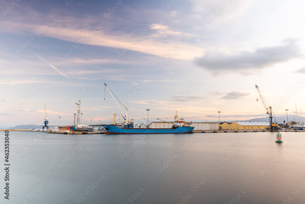 Long exposure  of Gandia's port in Valencia (Spain) at sunset, with views of ships and warehouses, and the sky with some clouds.