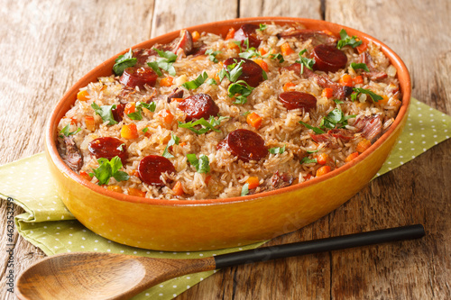 Authentic Arroz de pato duck rice is a traditional recipe from Portugal cooked with red wine, onion, carrot and chorizo close up in the baking dish on the wooden table. Horizontal