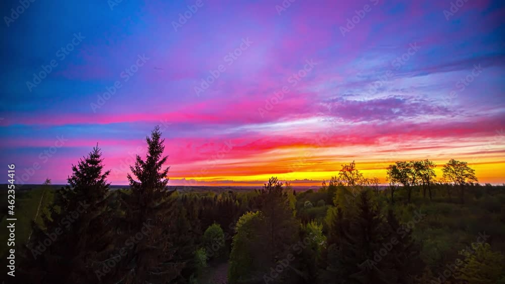 Time lapse of golden and blue hour with multi-colored clouds and at sky - Epic sunrise in rural landscape with trees and bush in foreground Time lapse of golden and blue hour with multi-colored clouds and at sky - Epic sunrise in rural landscape with trees and bush in foreground