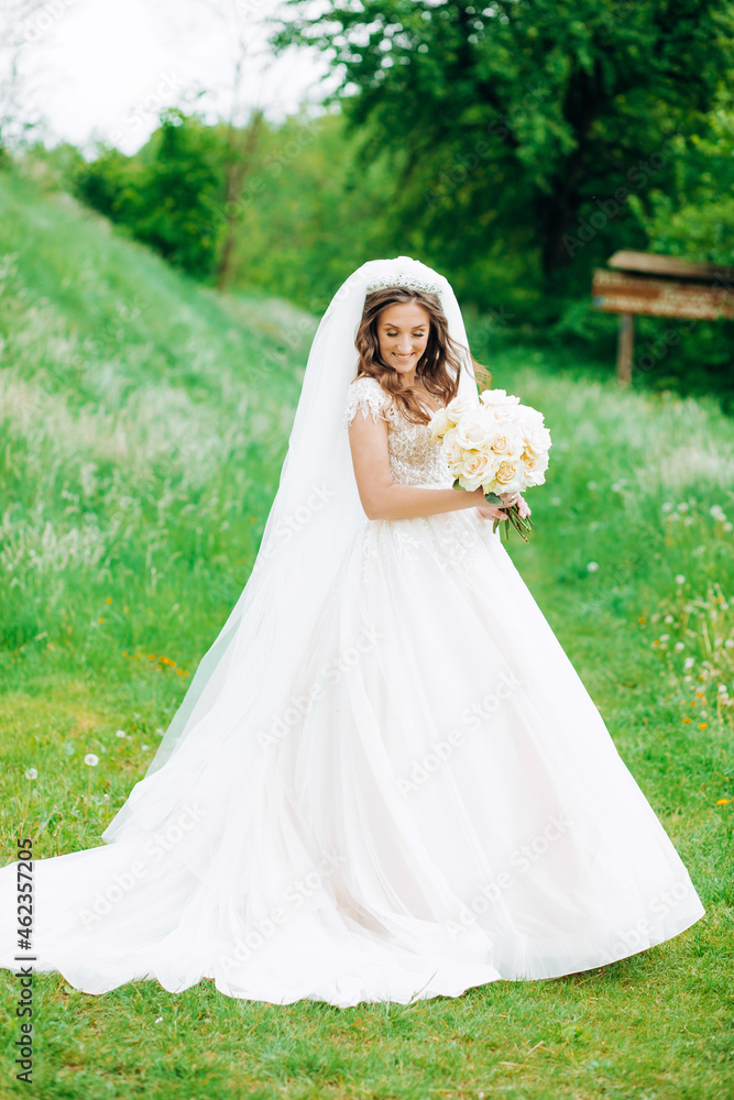 Amazing bride in a beautiful dress standing in the park holding a bouquet of roses in her hands. Amazing bride in a beautiful dress standing in the park holding a bouquet of roses in her hands.