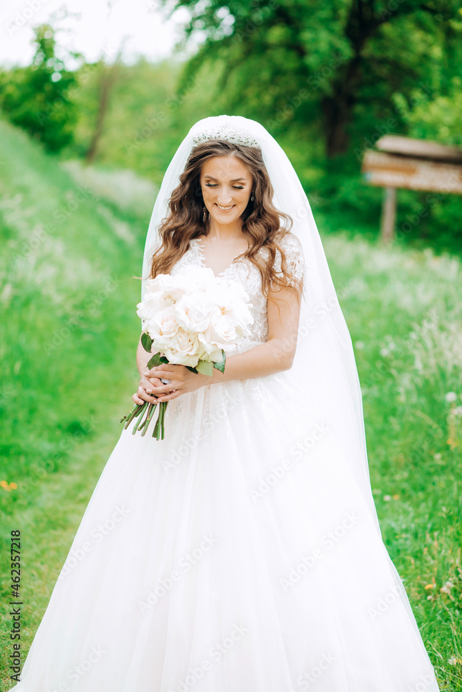 Sweet bride in a beautiful dress standing in the park holding a bouquet of roses in her hands. Sweet bride in a beautiful dress standing in the park holding a bouquet of roses in her hands.