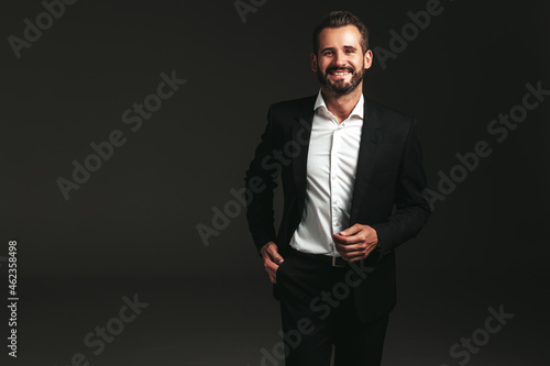 portrait of handsome smiling stylish hipster lambersexual model. Sexy modern man dressed in elegant black suit. Fashion male posing in studio on dark background. Looking at camera